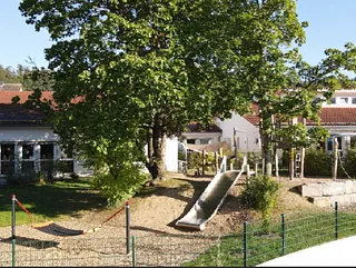 Ein Gebäude mit einem Spielplatz, Rutschen und einem großen Baum.