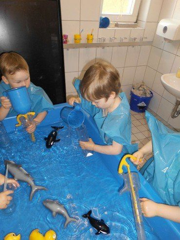 Kinder spielen mit Wasser und Spielzeug in einer blauen Wanne.