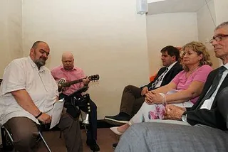 Gruppe von Erwachsenen in einem Raum, einer spielt Gitarre.