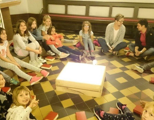 Kinder sitzen um ein leuchtendes Objekt.