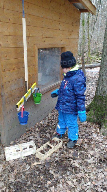 Kind spielt mit Eimern an einer Holzhütte.