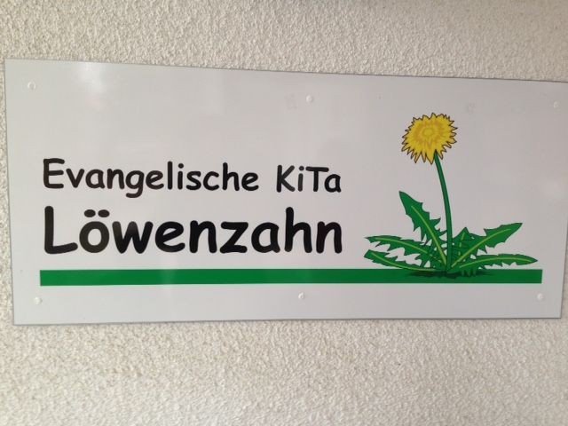 Schild mit Logo „Evangelische KiTa Löwenzahn“ und Pusteblume.