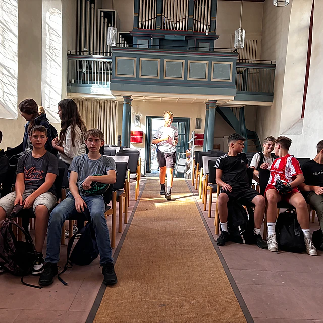 Jugendliche sitzen in einer Kirche auf Bänken.