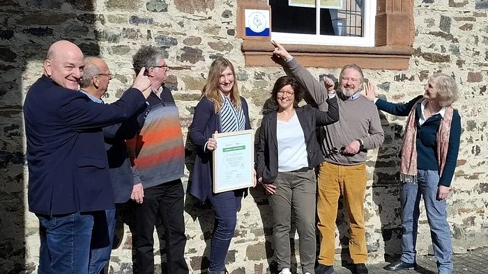 Gruppe lächelt und zeigt auf ein Schild an einer Wand.
