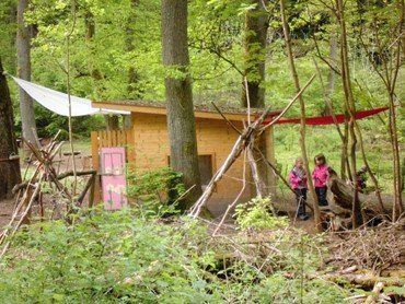 Holzhütte und Tipi-ähnliche Strukturen im Wald.