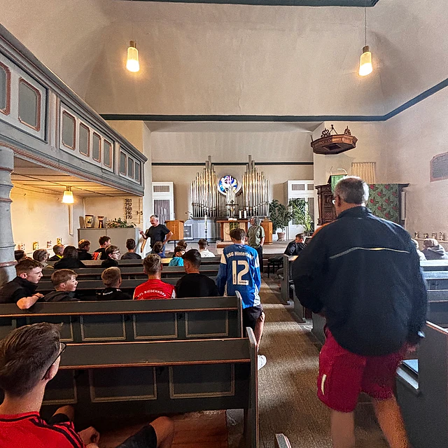 Innenansicht einer Kirche mit Holzbänken und Menschen.