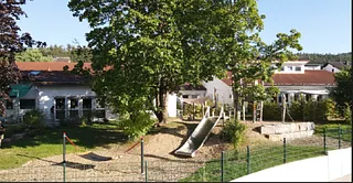 Ein Gebäude mit einem Spielplatz, Rutschen und einem großen Baum.