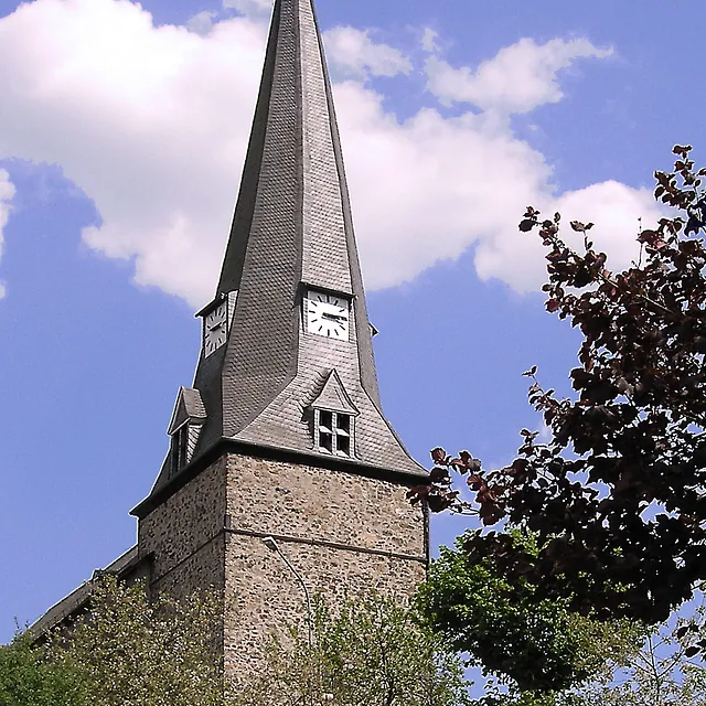 Kirchturm mit spitzem Dach unter blauem Himmel.