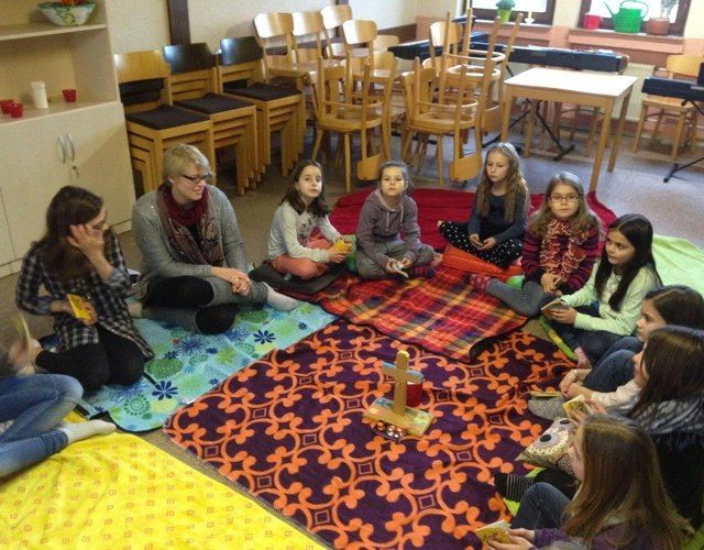 Kinder sitzen auf Teppichen in einem Kreis.