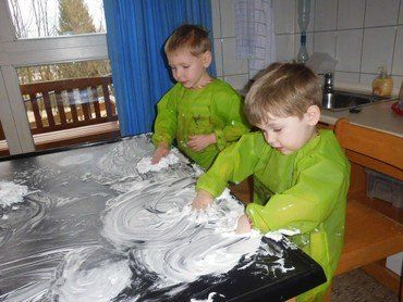 Zwei Kinder spielen mit Rasierschaum auf einem Tisch.