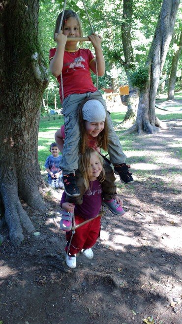 Drei Kinder spielen auf einer Schaukel.
