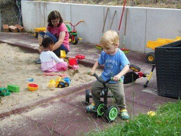 Kinder spielen in einem Sandkasten mit Spielzeug.