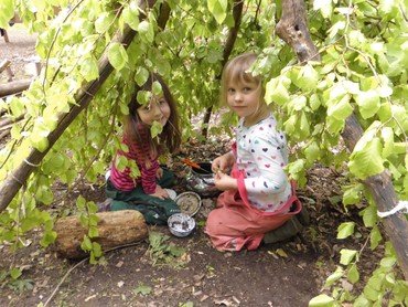 Zwei Kinder spielen in einer Blätterhöhle.
