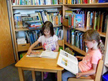 Zwei Kinder lesen in einer Bibliothek.