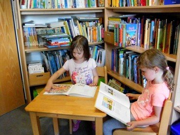 Zwei Kinder lesen in einer Bibliothek.