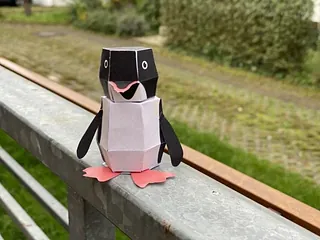 Papier-Pinguin auf Holzgeländer.