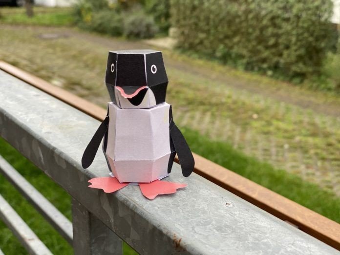 Papier-Pinguin auf Holzgeländer.